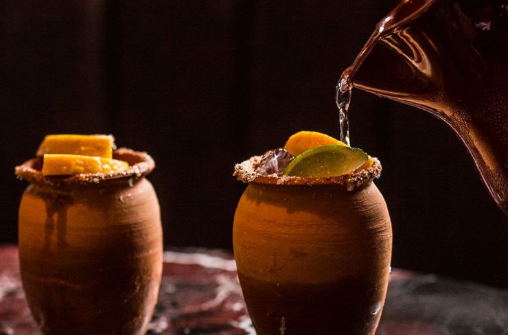 Cocktail being poured from a copper jug into stoneware cups.